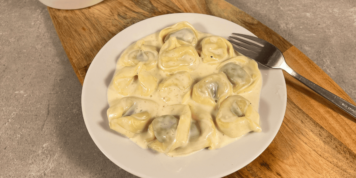 Das Bild zeigt Tortellini in Käse Sahne Soße auf einen Teller.
