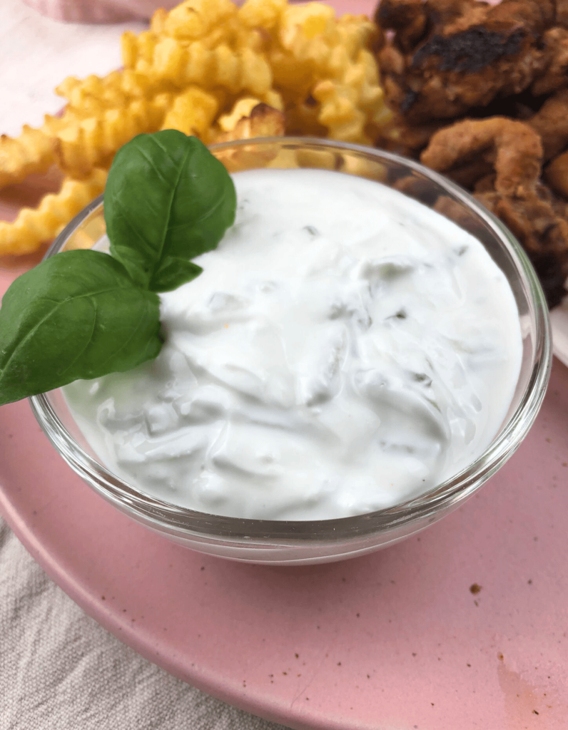 Cremiger Tzatziki in einer Schüssel angerichtet im Hintergrund sind Pommes und Gyros zusehen.
