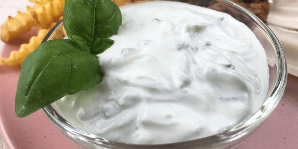 Frischer Tzatziki in einer Schüssel garniert mit einem Basilikum Blatt.