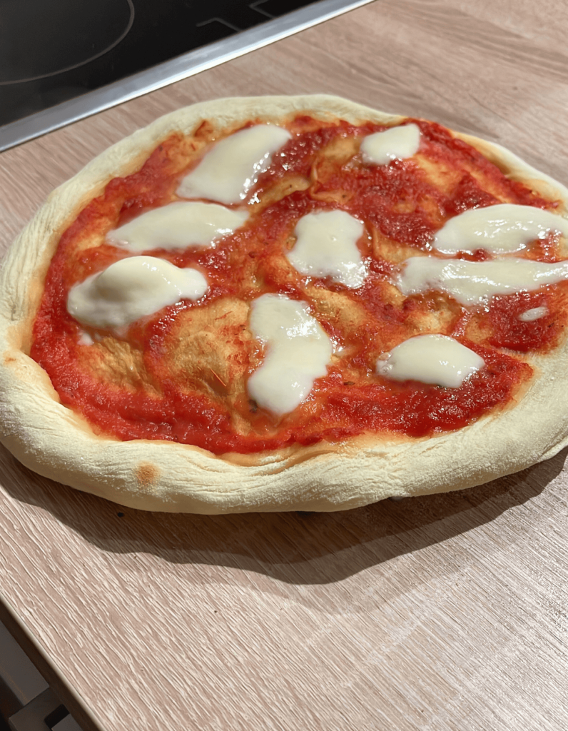 Das Bild zeigt eine vorgebackene Pizza mit Pizzasoße und geschmolzenen Mozzarella Käse die gerade abkühlt.