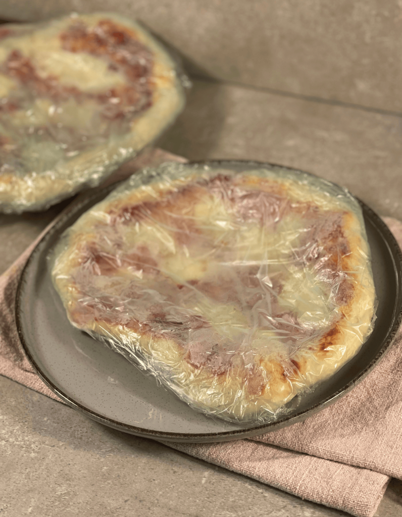 Das Bild zeigt eine eingefrorene Pizza eingewickelt in Frischhaltefolie.