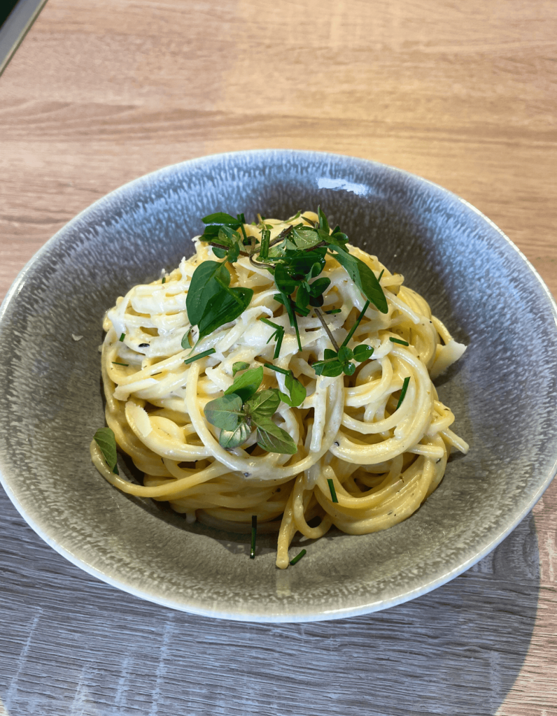 Nahaufnahme von dampfenden Spaghetti Carbonara ohne Speck, dekoriert mit fein gehackten Kräutern und geriebenem Käse.
