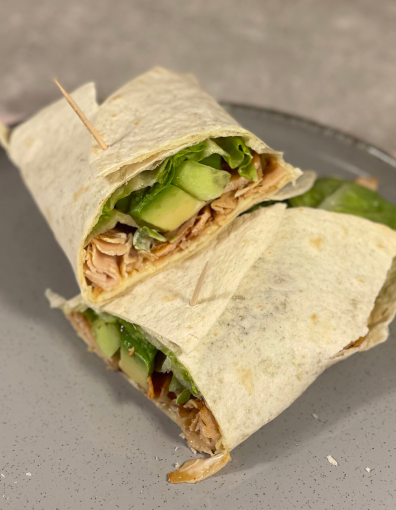 Frisch aufgeschnittener Wrap: Ein saftiger Hähnchen-Avocado-Wrap, mittig aufgeschnitten, zeigt die bunten Schichten aus Fleisch, Gemüse und geschmolzenem Käse.