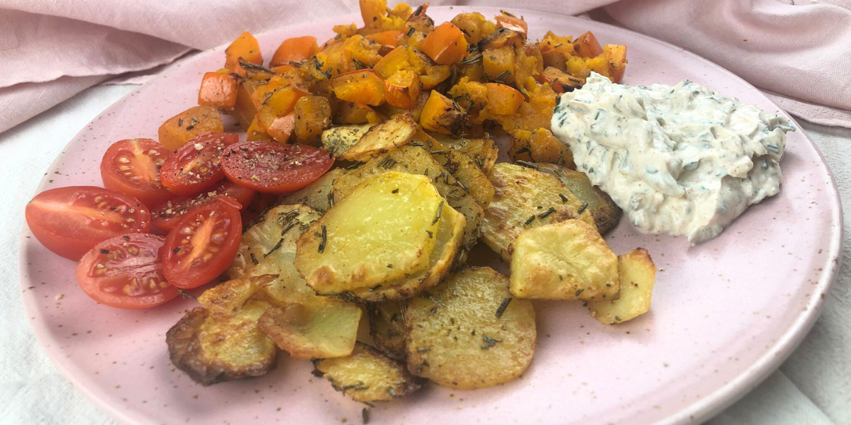Ein leckeres Herbstgericht: Kürbisstücke und Kartoffelscheiben aus dem Ofen, daneben eine Portion cremiger Quark-Dip mit frischen Kräutern.