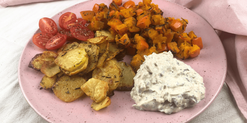 erösteter Kürbis und Kartoffeln mit einer leichten Bräune, angerichtet neben einem Kräuterdip, der mit frischem Dill verfeinert ist.