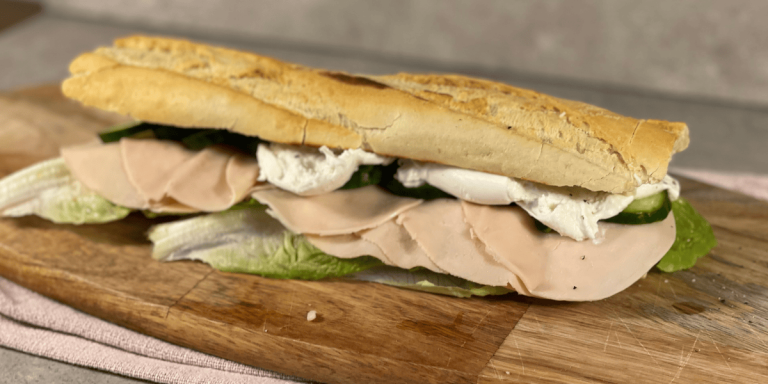 Frisch angerichtetes Baguette auf einem Holzbrett, Burrata tropft zart herunter.