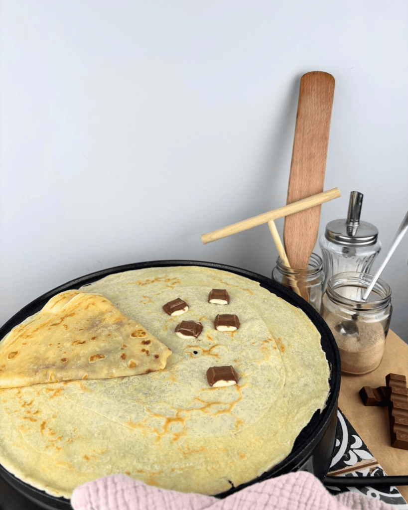 Das Bild zeigt einen Crepe, der mit geschmolzenen Kinderschokoladenstücken belegt ist, wodurch eine verlockend süße Füllung entsteht.