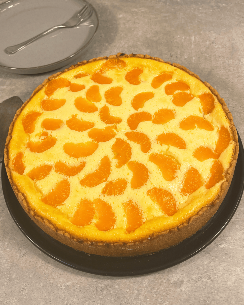 Das Bild zeigt einen ganzen Mandarinen Käsekuchen auf einem Teller.
