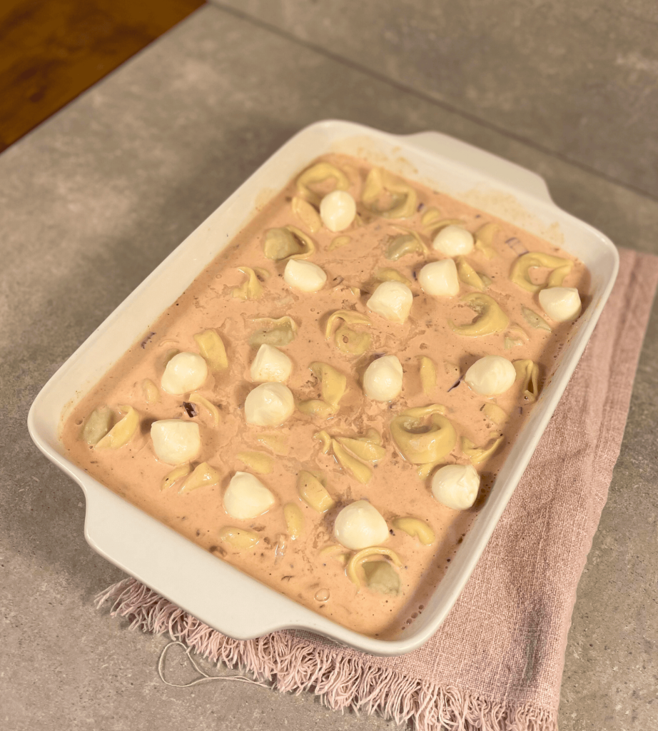 Ein Tortellini Auflauf mit cremiger Tomaten-Sahne-Soße und Mozzarella Kugeln bereit für den Backofen.