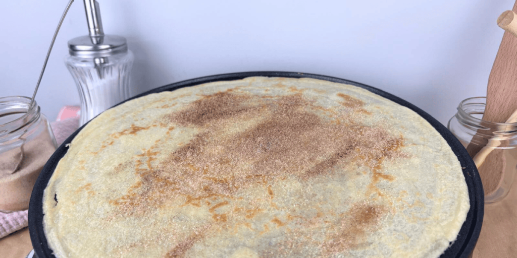 Das Bild zeigt einen Crepe, der mit Zimt und Zucker bestreut ist und bereit liegt, um zusammengeklappt zu werden.