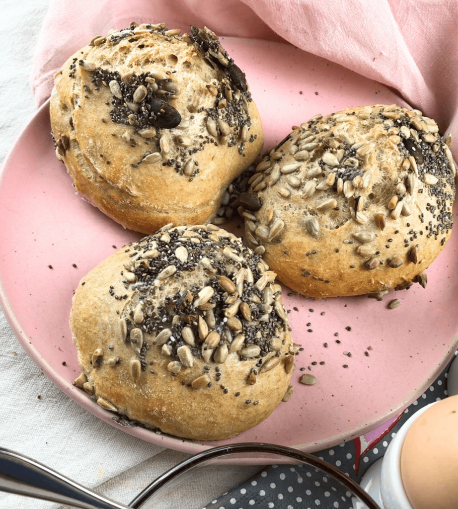 Drei leckere Weizenvollkorn Brötchen mit Sonnenblumenkernen auf einen Rosa Telle.