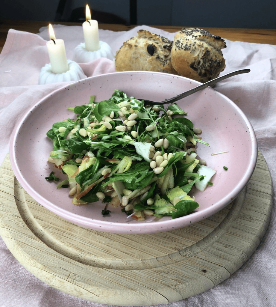 Ein knackiger Feldsalat mit Apfel und Pinienkernen serviert in einer Rosa Schüssel