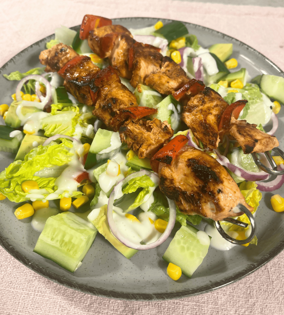 Ein Teller mit einem bunten Salat und zwei Hähnchenspießen.