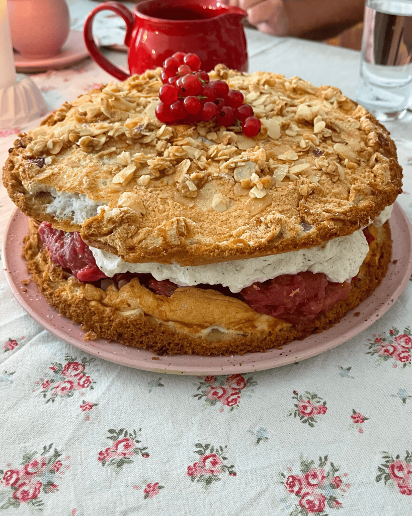 Eine selbstgemachte Rhabarbertorte mit Sahne auf einen gedeckten Tisch. 